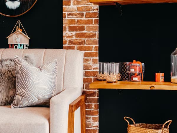 Sofa with a patterned cushion, brick wall, and a wooden shelf displaying glasses and candles.